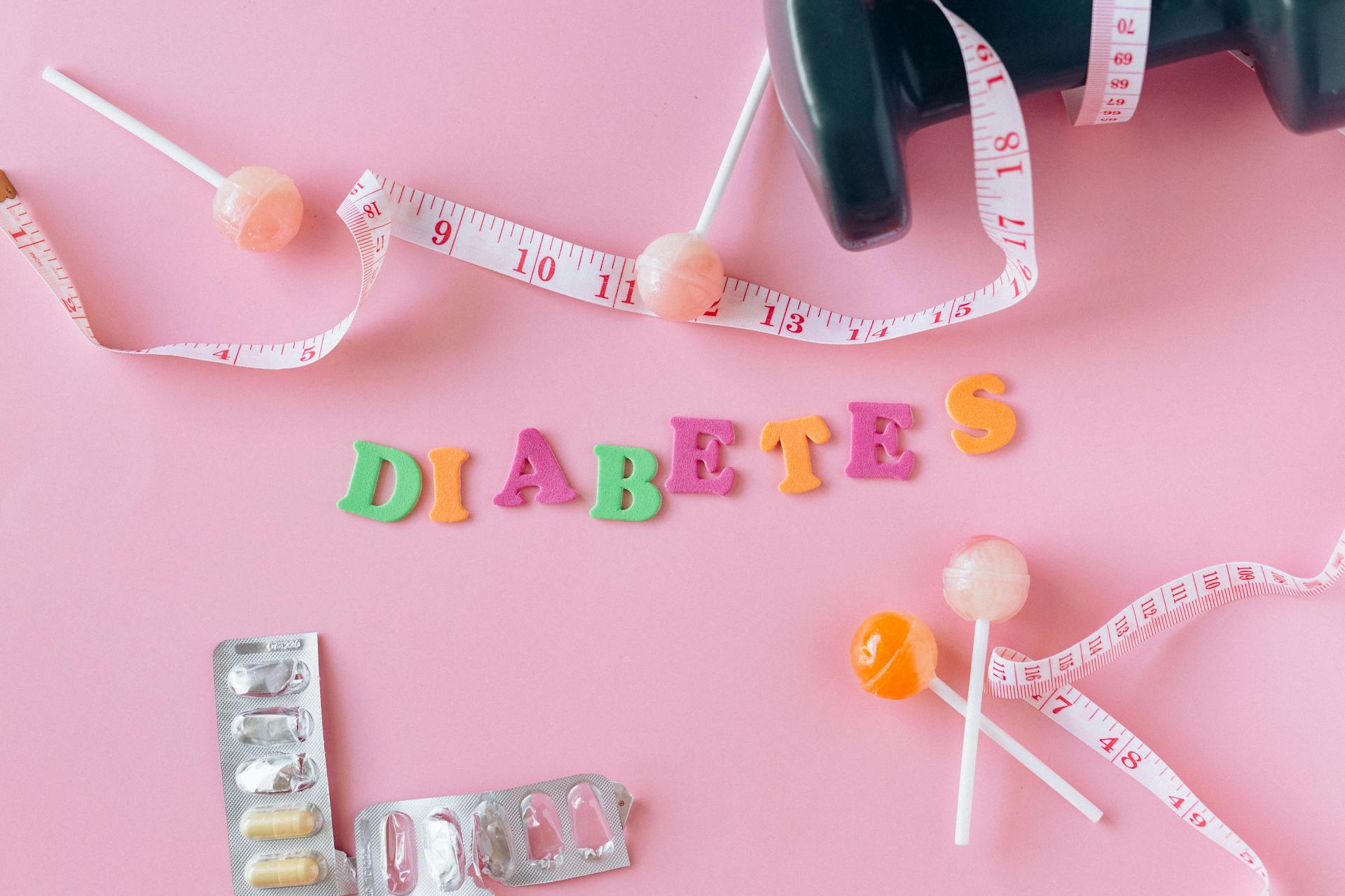 Lollipops, Meter and Medicaments on a Pink Background around Letters Creating a Word Diabetes