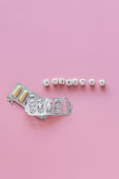 Top view of diabetes pills and letter tiles on pink background, symbolizing health awareness.
