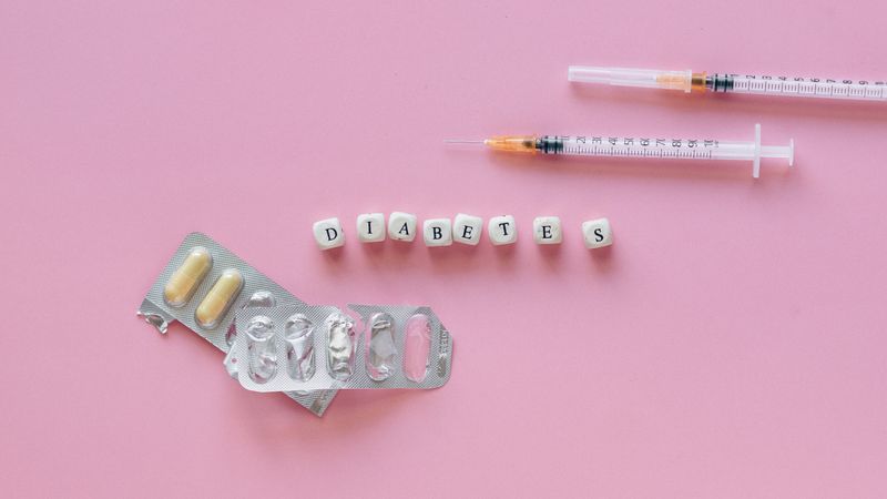 Flat lay of diabetes medication symbolized with pills and syringes on a pink background.