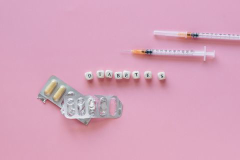 Flat lay of diabetes medication symbolized with pills and syringes on a pink background.