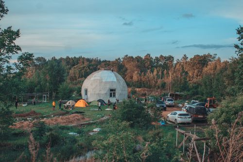 Free A rustic dome house with camping tents and vehicles in a scenic woodland setting. Stock Photo