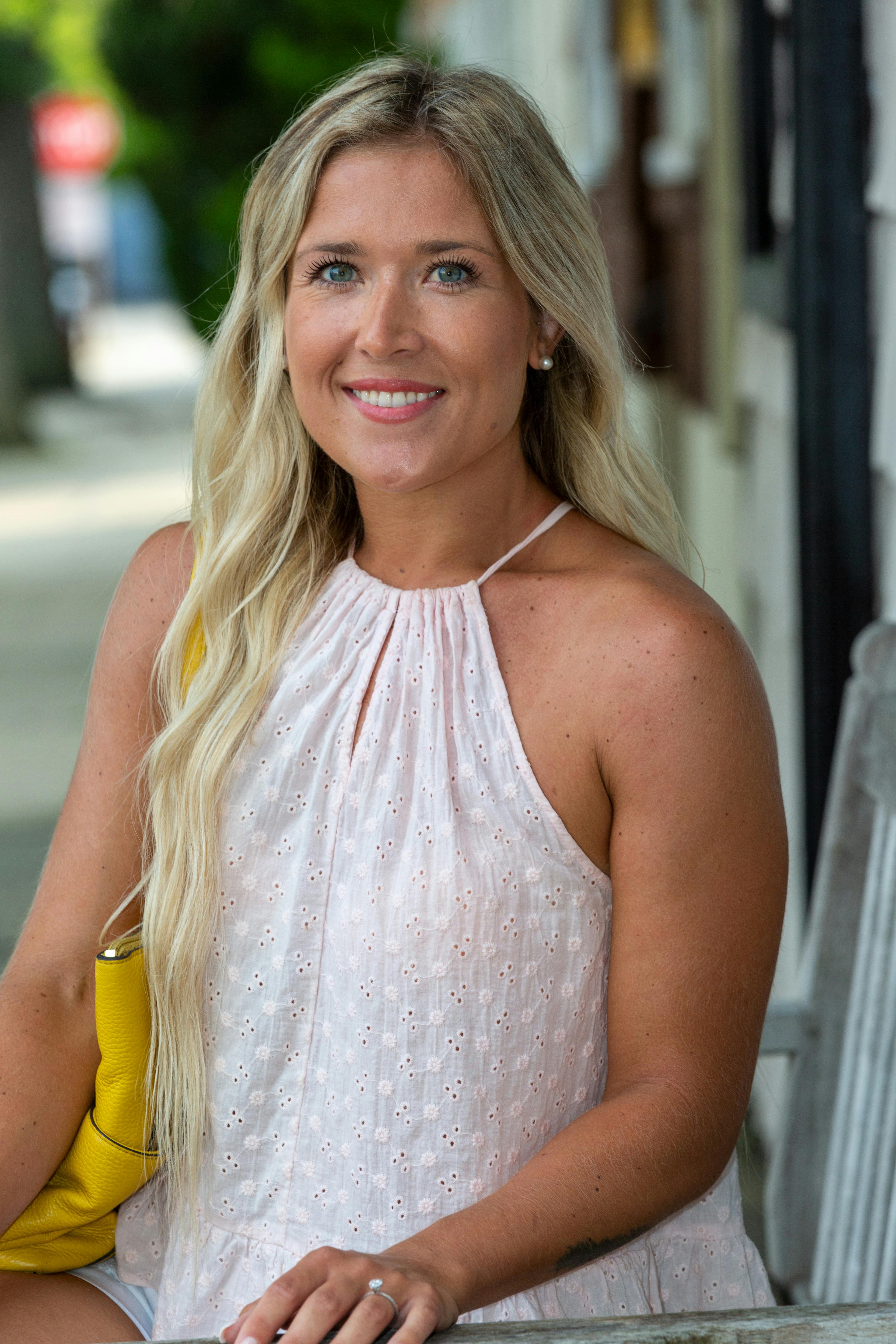 A cheerful woman sitting outdoors in a light blouse, enjoying a sunny day.
