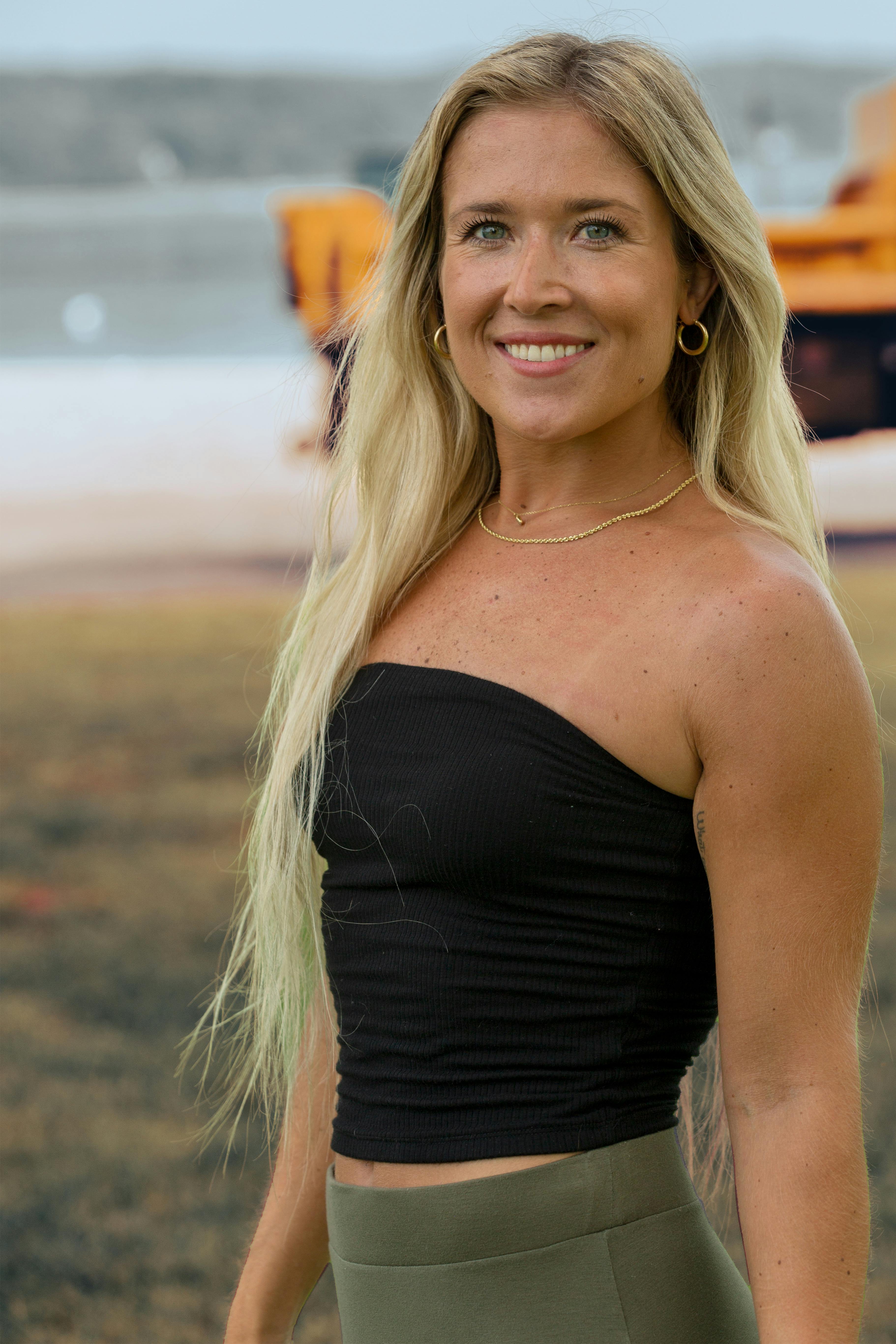 Blonde woman with a smile standing outdoors in a black tube top. Capturing a sunny day.