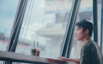 一个年轻人独自坐在咖啡馆的大窗边喝咖啡