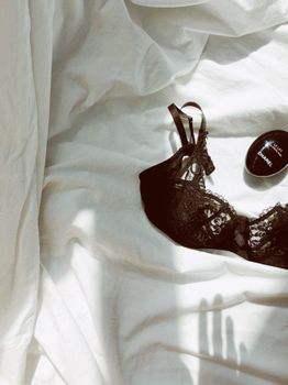 A stylish black lace bra and Chanel beauty product elegantly placed on soft white bedding under natural light.