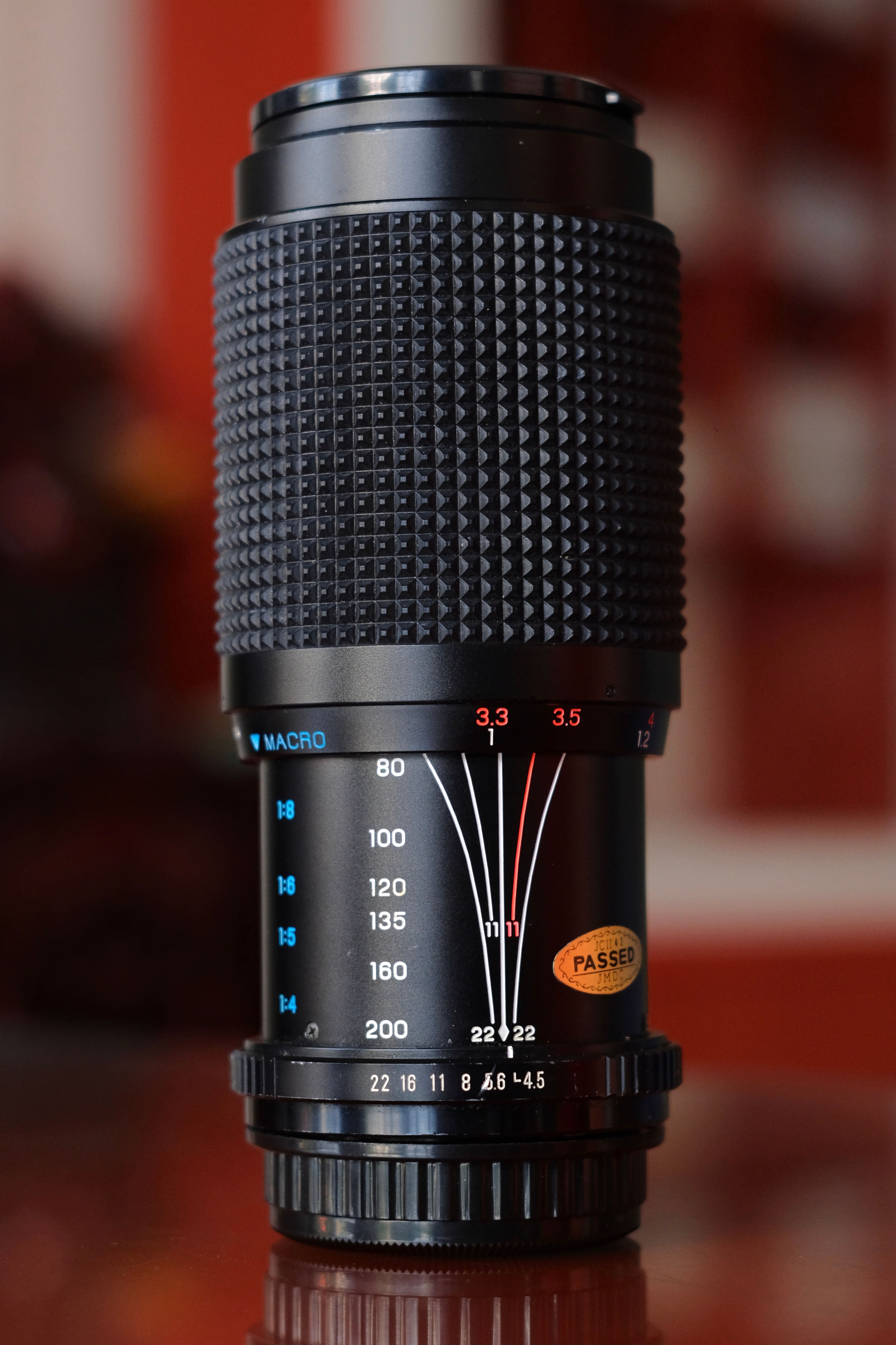 Detailed close-up of a telephoto camera lens with macro focus settings and blurred background.