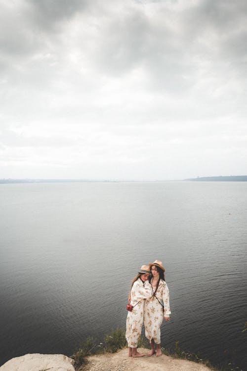 Free Women in Floral Dress Embracing Each Other while Standing on the Cliff Near the Ocean Stock Photo