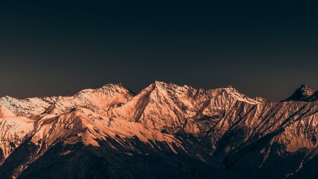 Majestic snow-covered mountains illuminated by sunset, creating a serene and dramatic landscape.