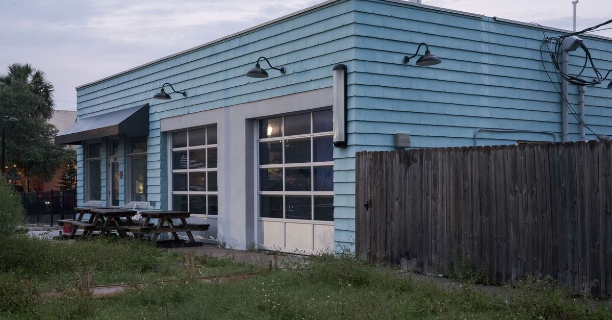 A turquoise industrial building with wooden fence and picnic tables under an overcast sky.
