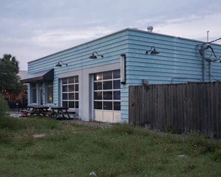 A turquoise industrial building with wooden fence and picnic tables under an overcast sky.