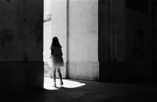 Free A woman in a dress stands in the shadow of a sunlit urban archway. Stock Photo