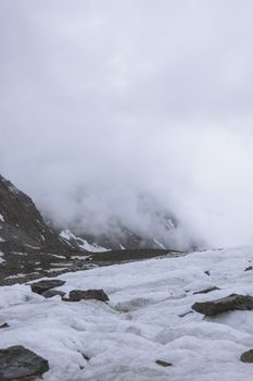 Fog envelops a snow-covered mountain, creating a dramatic winter scene with rocky formations.