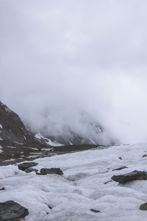 Free Fog envelops a snow-covered mountain, creating a dramatic winter scene with rocky formations. Stock Photo