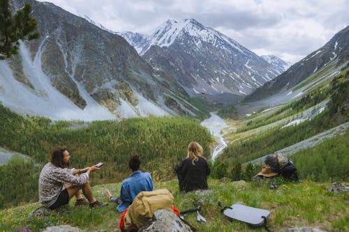 People Sitting on Green Grass Near Gray Mountains