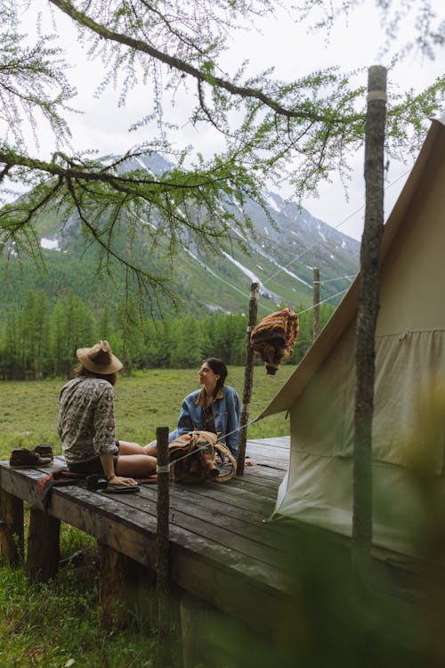 Couple Sitting by the Tent on a Wood by the Landscape of a Mountain and Meadow