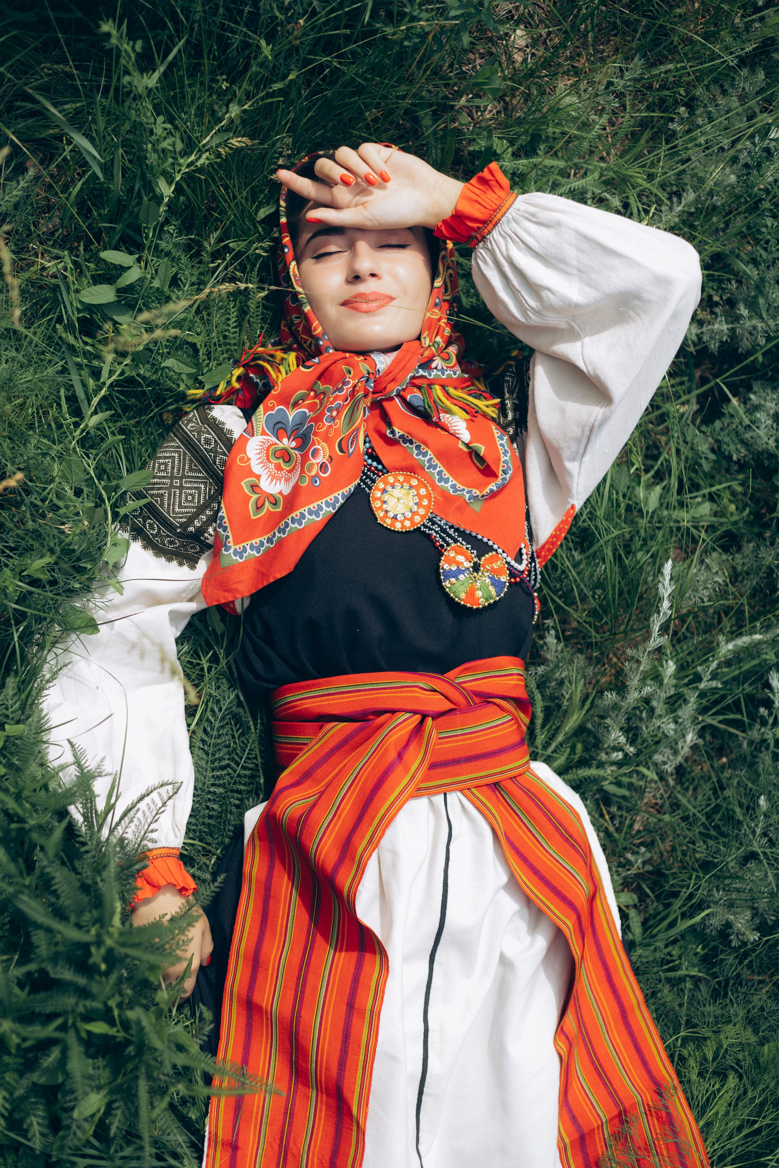 Woman in colorful traditional attire relaxing on green grass, enjoying sunlight.