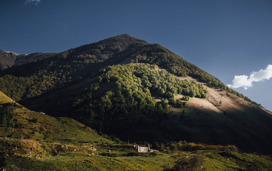 Dramatic landscape of lush green hills and mountains under a blue sky in Karachay-Cherkessia, Russia.