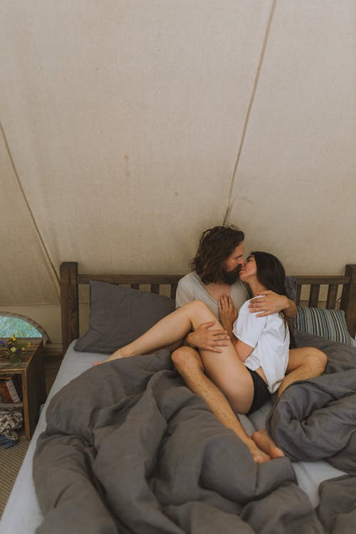 A Couple Sitting on the Bed while Kissing Each Other