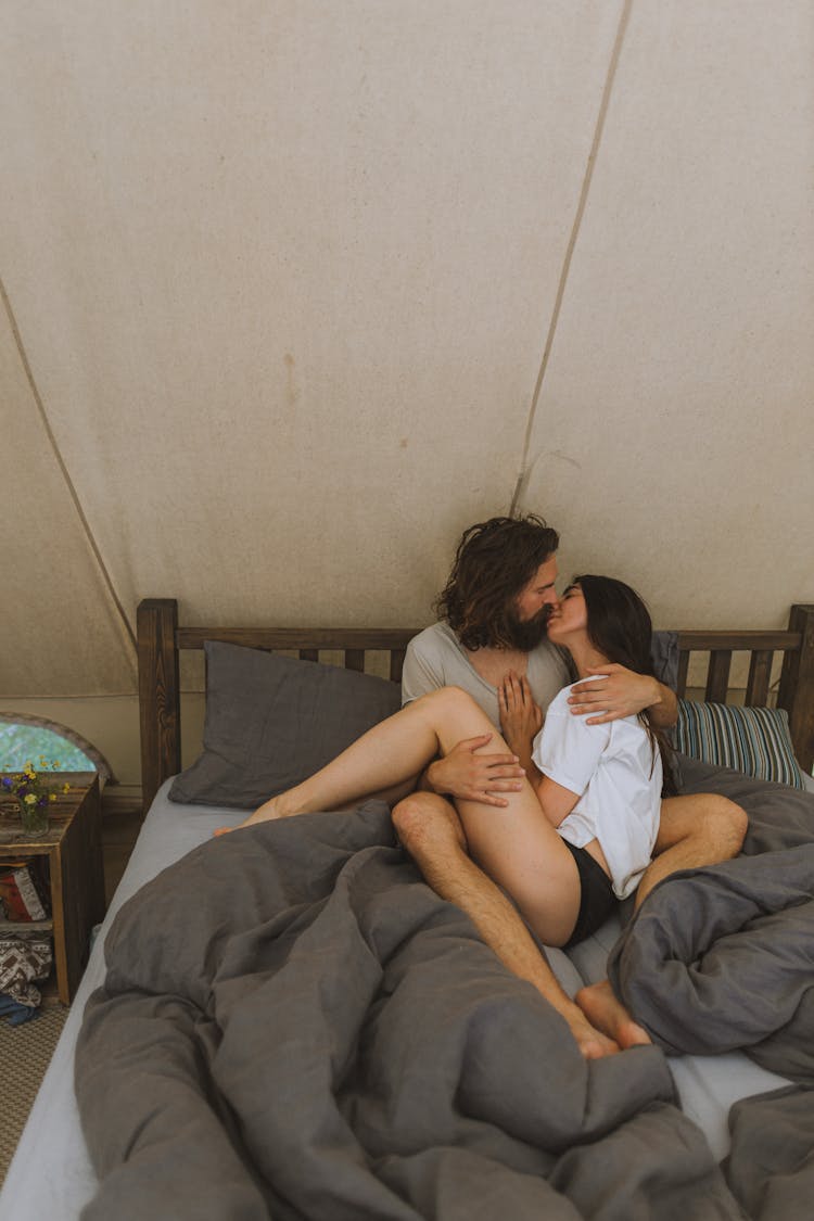 A Couple Sitting On The Bed While Kissing Each Other