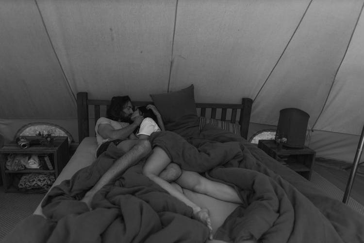 A Grayscale Photo Of A Couple Lying On The Bed While Kissing Each Other