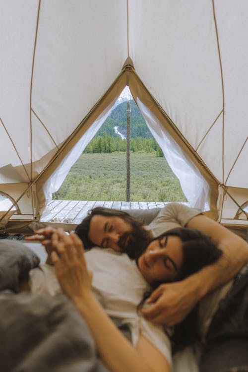 Free Couple relaxing in a tent with a beautiful mountain view, symbolizing outdoor romance and adventure. Stock Photo