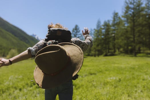 A hiker with a hat runs joyfully through a lush green meadow under a clear blue sky.