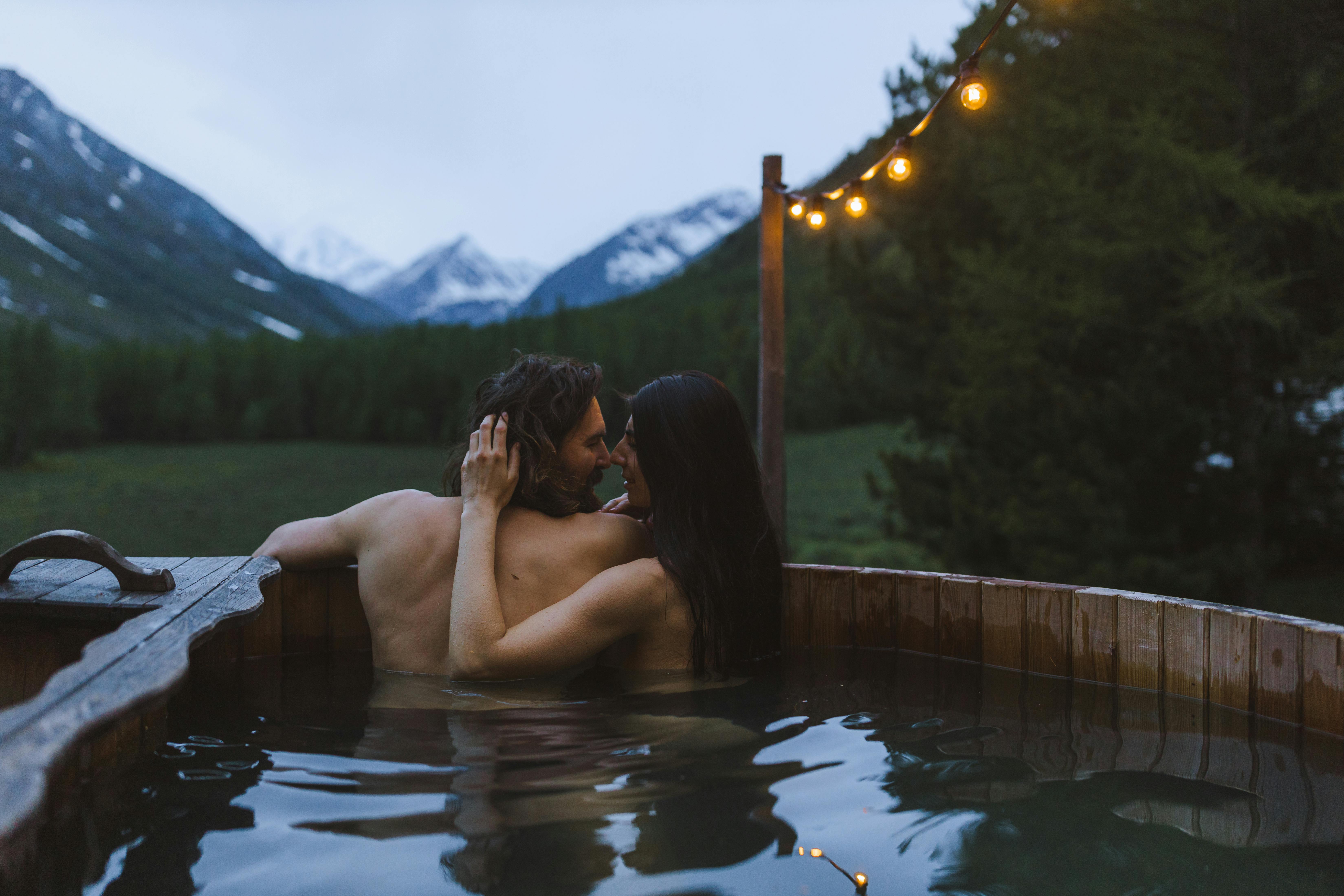 couple hugging in a wooden bath with a view on the landscape of the mountains and a forest