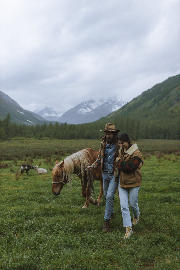 Man And Woman Walking With Horse On Grass Field