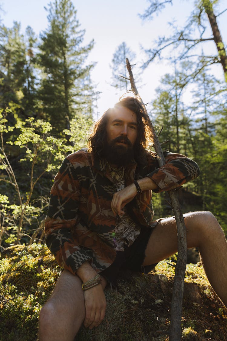 Man Holding A Stick Sitting On Dirt Ground