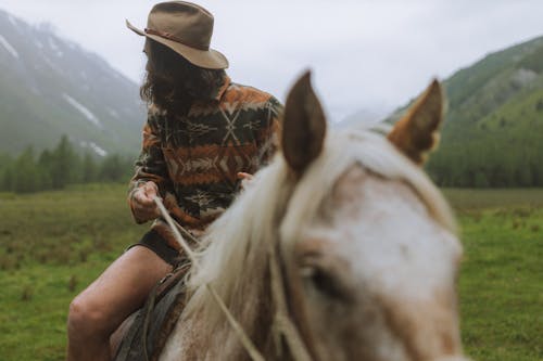 Brunette Man in a Beige Hat Riding a Horse in the Mountains