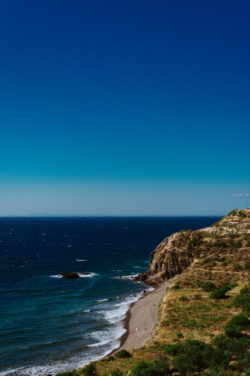 Free Breathtaking view of the ocean waves crashing against rugged coastal cliffs under a deep blue sky. Stock Photo