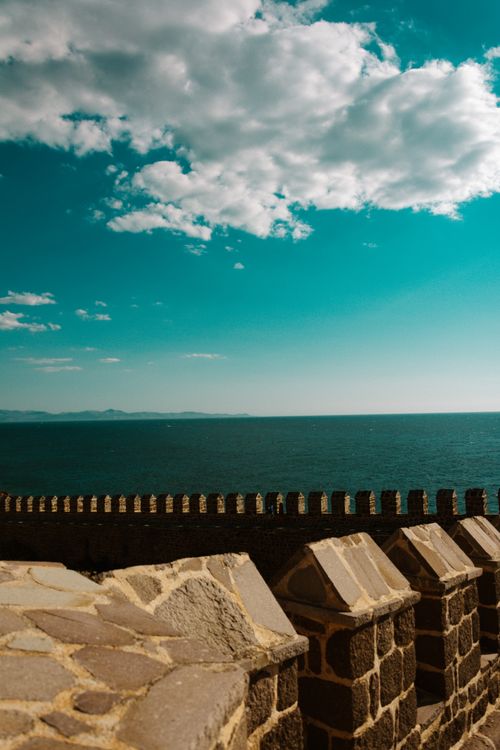 Free Scenic view of a stone wall overlooking the sea under a cloudy sky, creating a dramatic atmosphere. Stock Photo