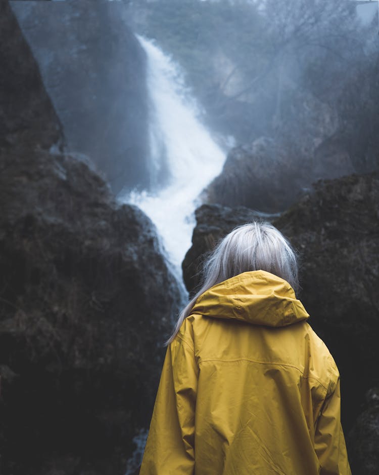 Back Of A Woman Wearing A Raincoat Hiking By A Rock Formation