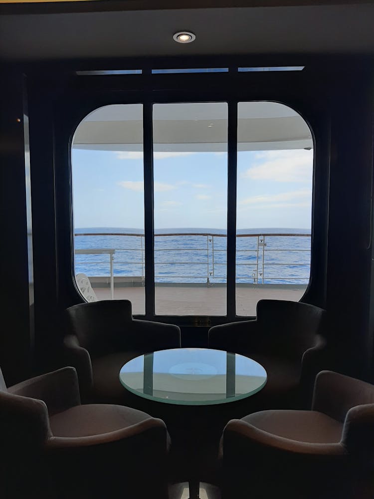 Table With Armchairs Inside A Cruiseship With A View On The Sea From The Window