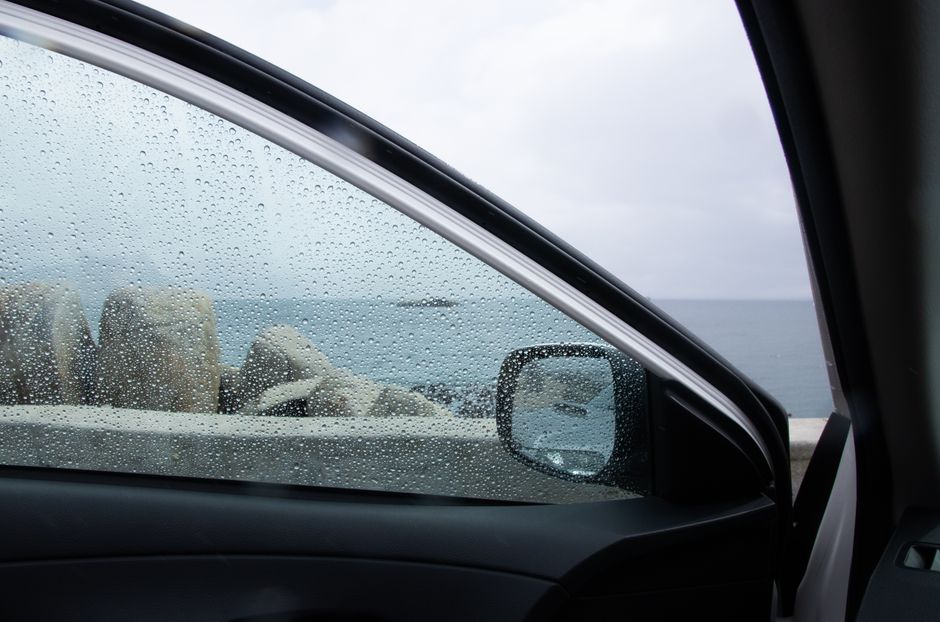 Glistening water droplets on a car window with a scenic ocean backdrop.
