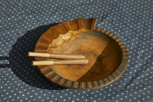 Close-up image of a rustic ashtray holding cannabis joints on a patterned background.