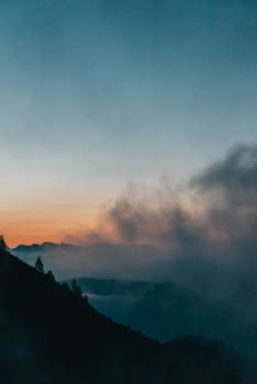 Peaceful mountain scene at sunrise with clouds and silhouette of peaks.
