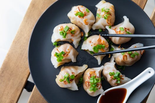 Close-up of delicious steamed dumplings on a black plate with soy sauce, garnished with fresh greens.