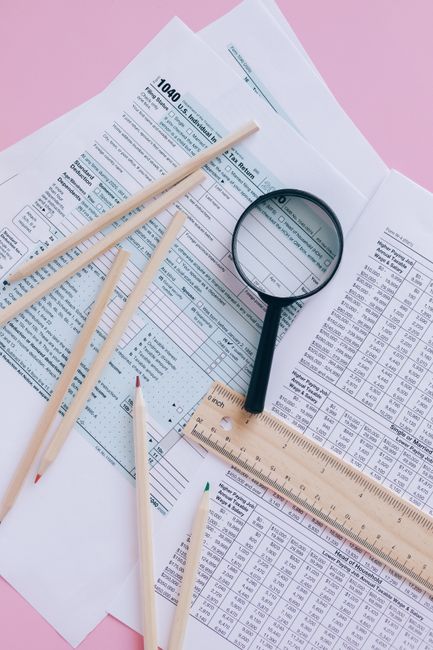 Tax documents with magnifying glass and pencils on a pink surface. Tax documents with magnifying glass and pencils on a pink surface.