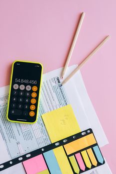 A vibrant workspace with a smartphone and tax documents on a pink background.
