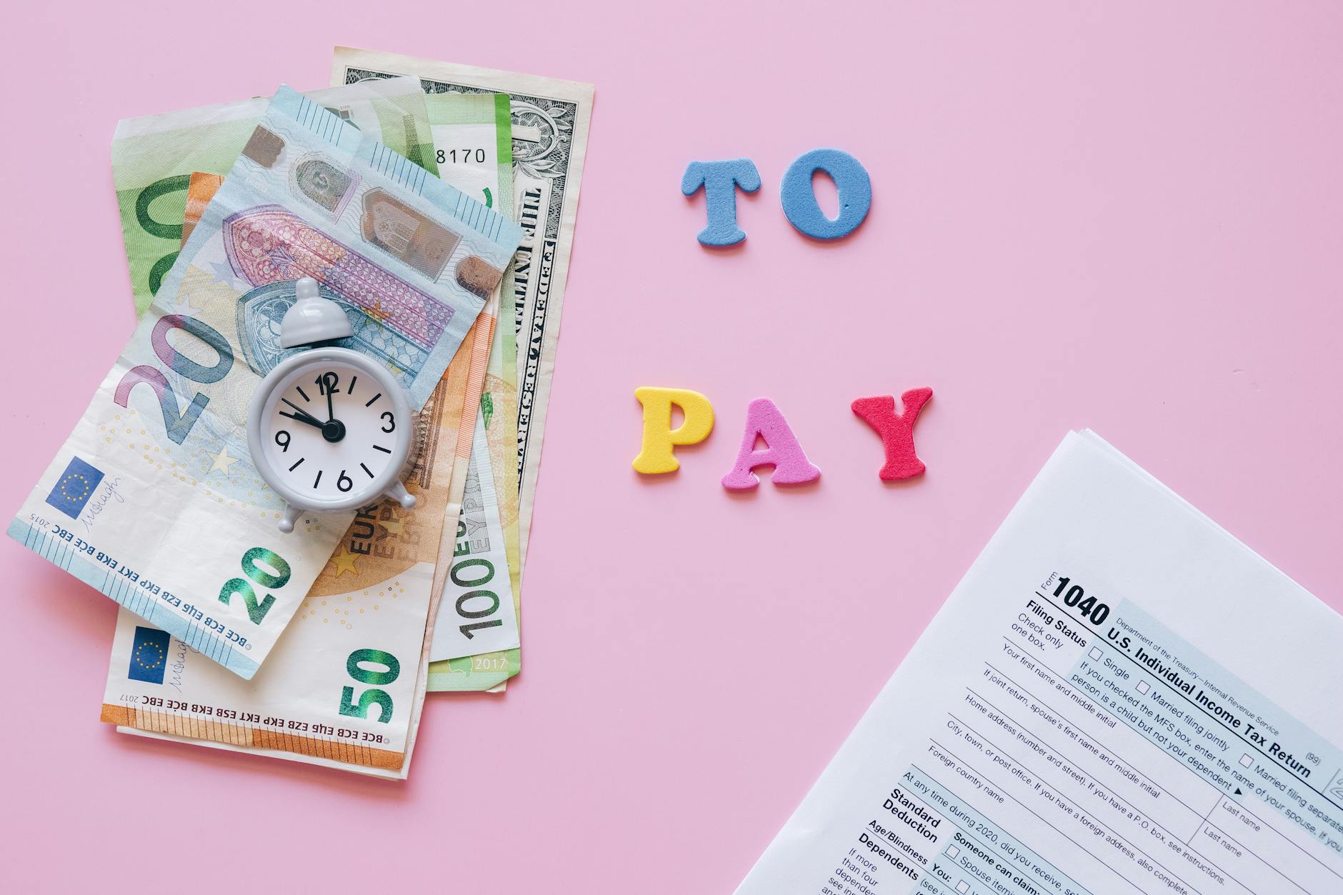 Flat lay of taxes, currency, and reminder to pay on pink background.