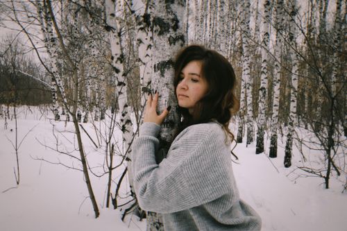 Free A woman embraces a birch tree in a snowy forest, capturing a serene winter moment. Stock Photo