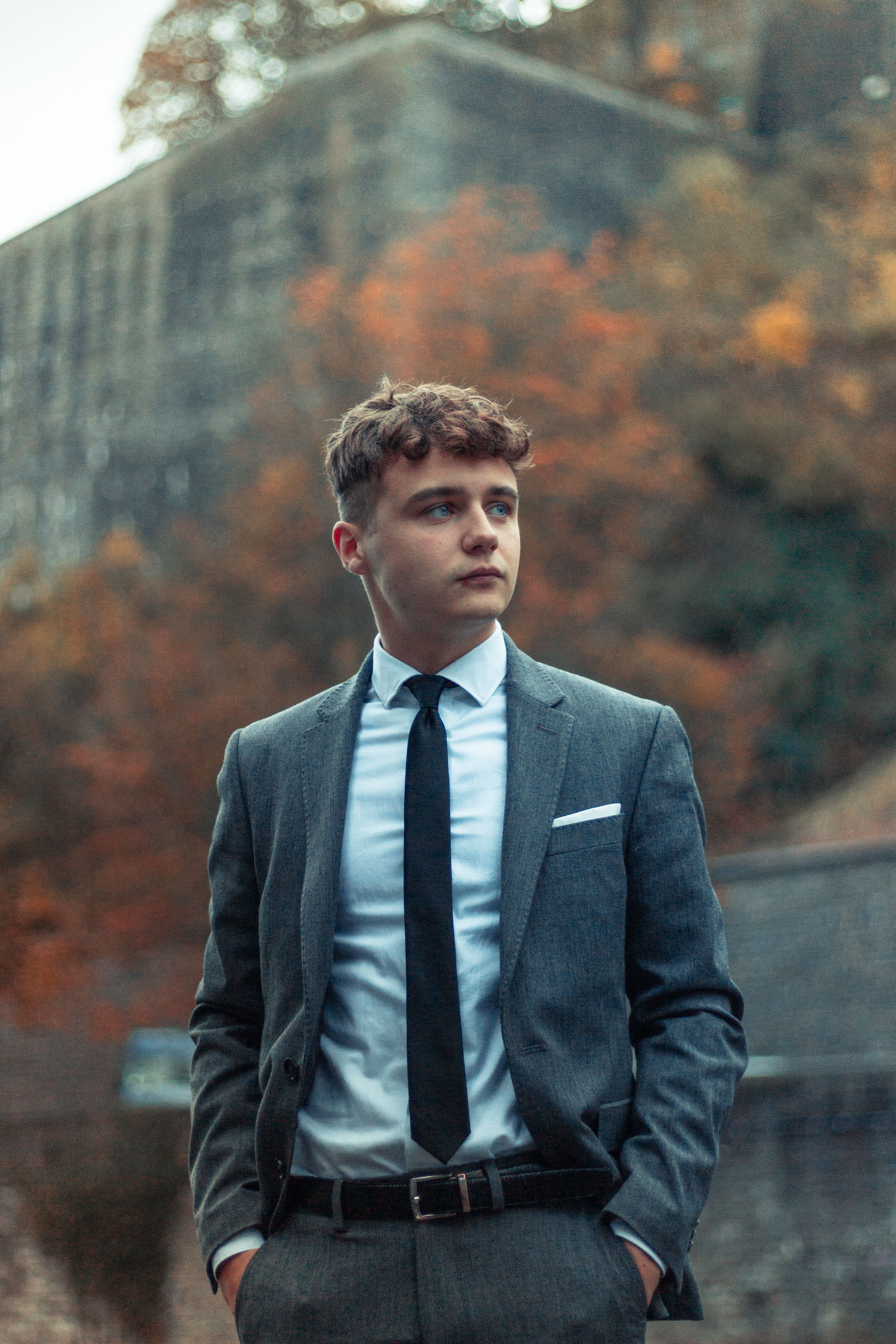 Stylish young man in a suit with autumn leaves background, hands in pockets.