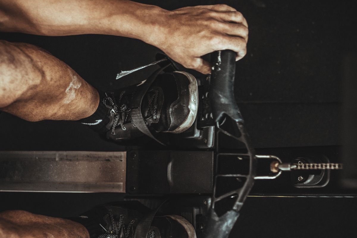 A close-up shot of a man using a rowing machine indoors, focusing on footwear and equipment