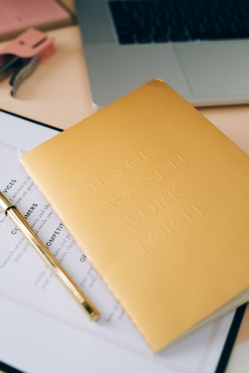 Free A stylish office desk with a motivational notebook, laptop, and stationery, promoting productivity. Stock Photo