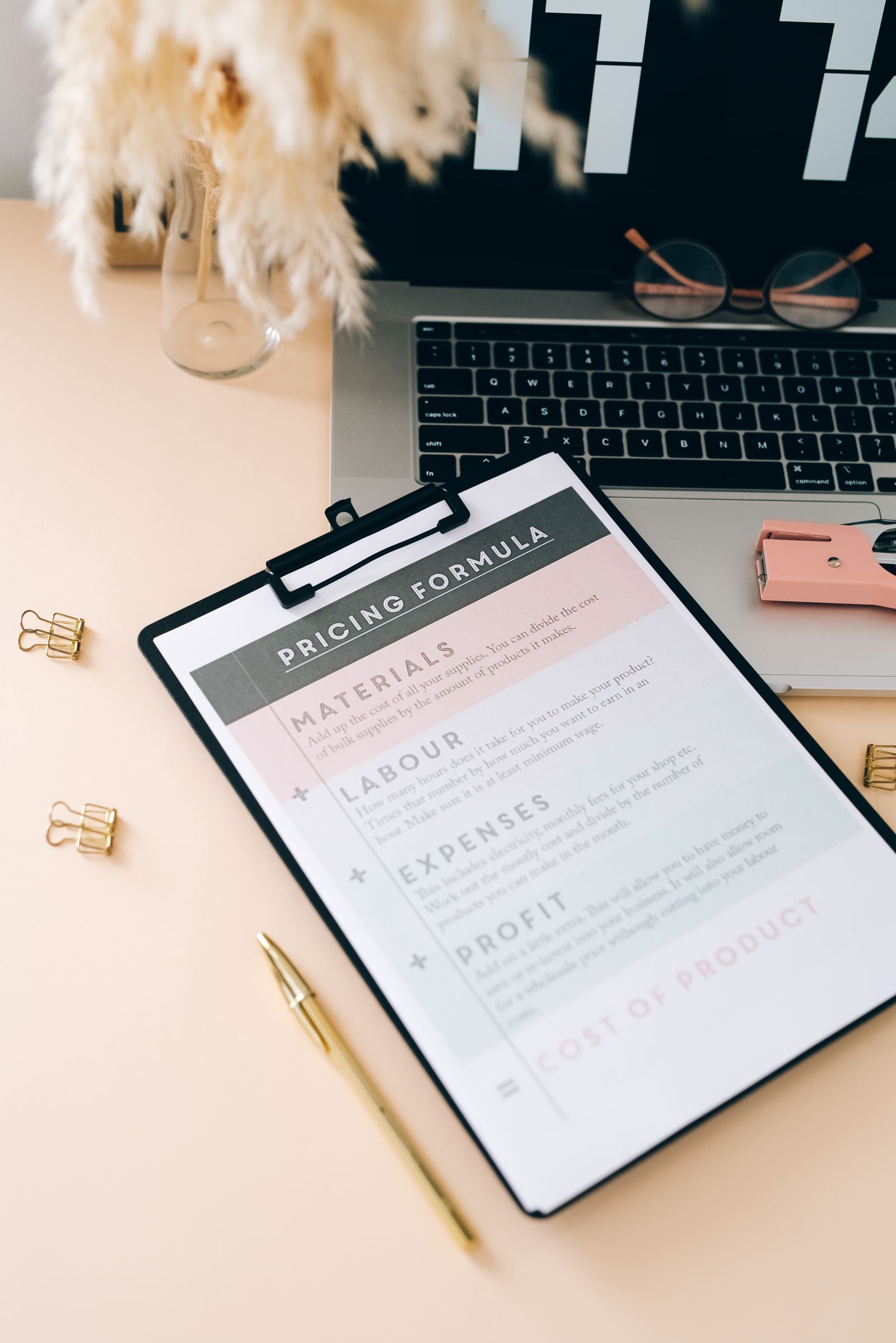 A pricing worksheet on a clipboard next to a laptop on a desk