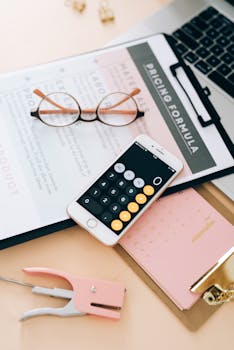 Flat lay of business tools including smartphone, calculator, and eyewear on a desk.