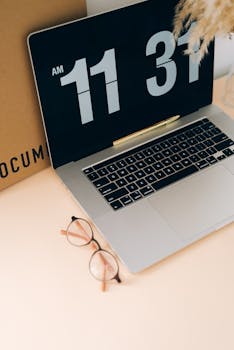 A tidy workspace showcasing a MacBook with digital clock display and eyeglasses on a desk.