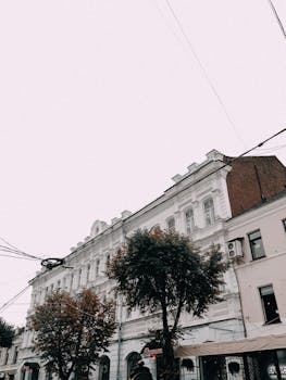Low angle view of classic European-style buildings with trees and clouded sky.