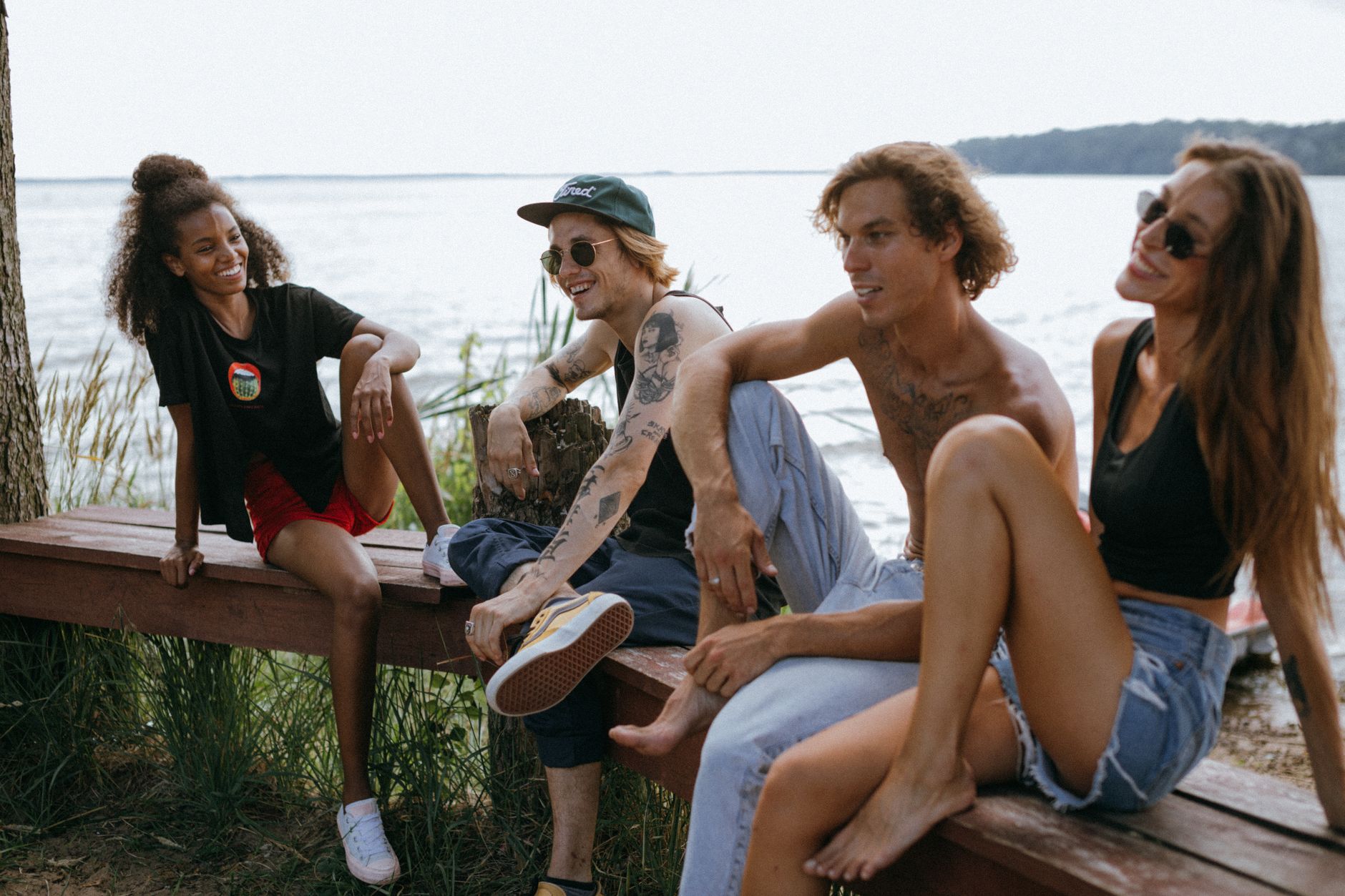 A diverse group of young friends laughing and relaxing by the lakeside on a wooden bench.